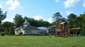 A grassy field with a wooden play structure and a house with a sloped roof and solar panels.
