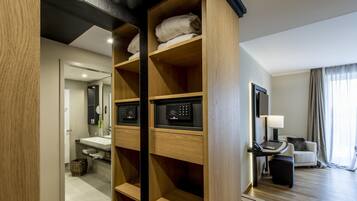 A modern hotel room with a wooden wardrobe, a vanity with a mirror, a small table with a lamp, and a sofa.