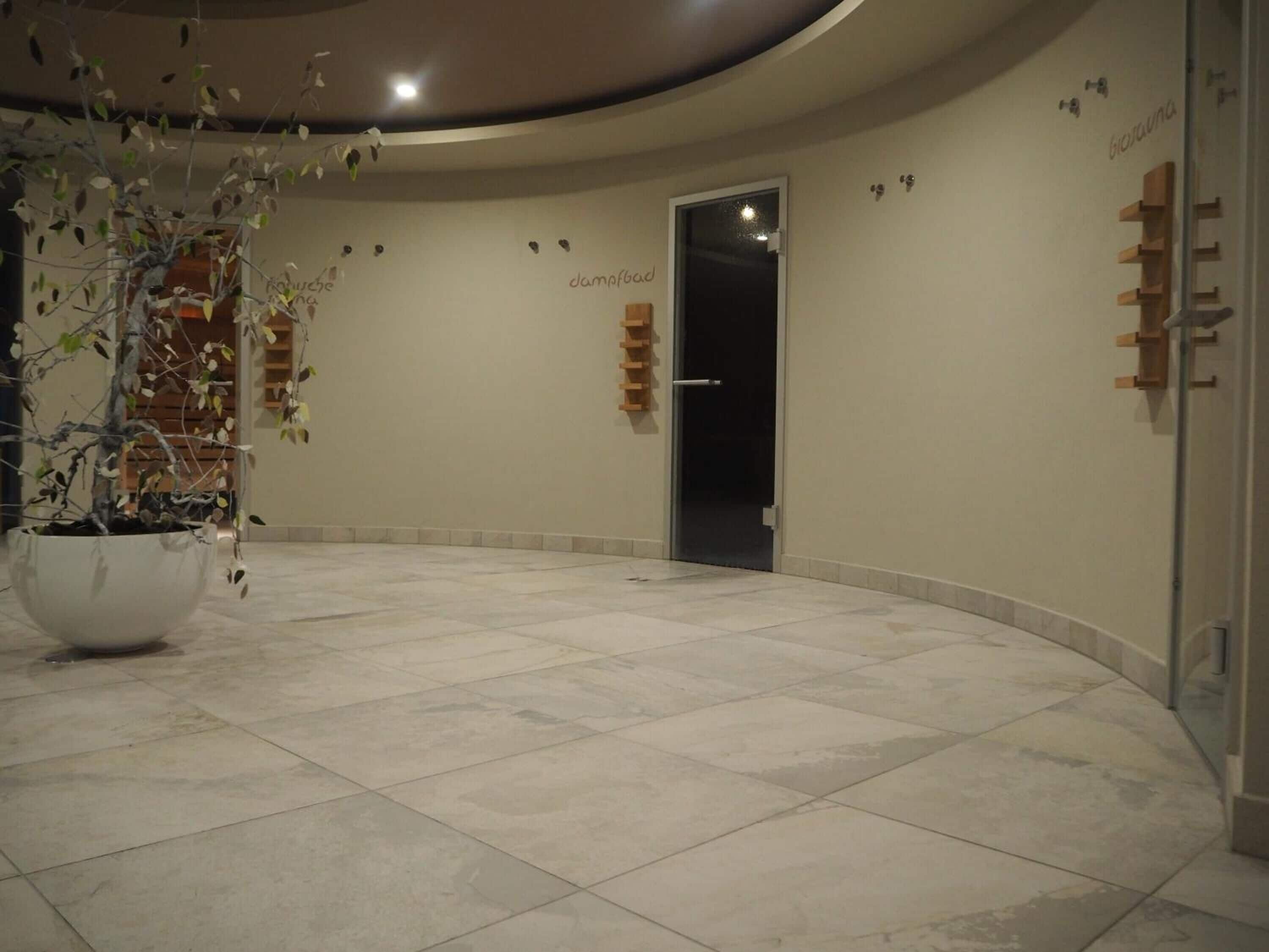 Eine geräumige Lobby mit einer großen Topfpflanze, einer Tür mit der Bezeichnung 'dampfbad' und einem an der Wand befestigten Regal mit Gegenständen.