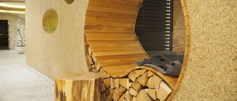 Estructura circular de madera con zona de estar y un montón de leña en el interior.