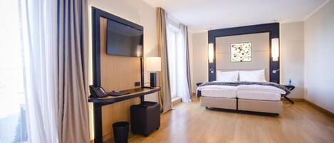 Una habitación de hotel moderna con cama, mesita de noche, lámpara y un ventanal con cortinas.