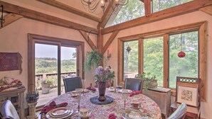 Un comedor con una mesa redonda dispuesta para seis personas, rodeada de sillas de madera. Hay un ventanal con vistas a la vegetación.