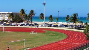 Pista de corrida com superfície vermelha, um poste de gol e um campo gramado.