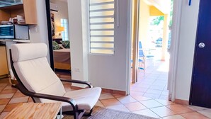 A modern living room with a white leather chair, a small wooden table, and a sliding glass door leading to an outdoor patio area.