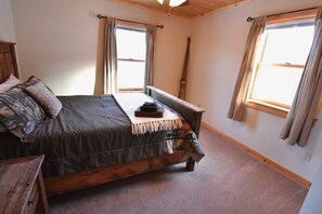 Un dormitorio con una cama grande, cabecero de madera y dos ventanas con cortinas.