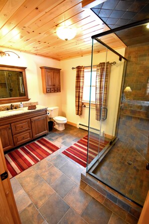 Un baño con tocador de madera, cabina de ducha de vidrio y alfombra roja a rayas.