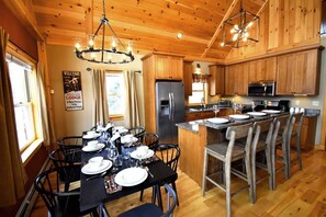 Una cocina de estilo cabaña de madera con una isla central, una mesa de comedor preparada para seis comensales y un refrigerador.