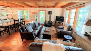 A cozy living room with a fireplace, leather sofas, a dining area with a glass table, and large windows offering a view of the outdoors.