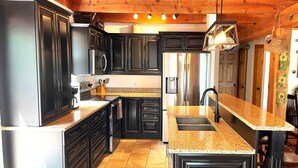 A kitchen with dark cabinetry, granite countertops, stainless steel appliances, and a hanging light fixture.