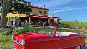 A red vintage convertible car parked in front of a yellow building with outdoor seating.