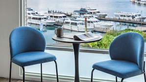 A room with two blue chairs, a small table with a book and a mug, and a view of a marina with boats. - Shui Yang Lakeview House with Elevator (Yuchi)