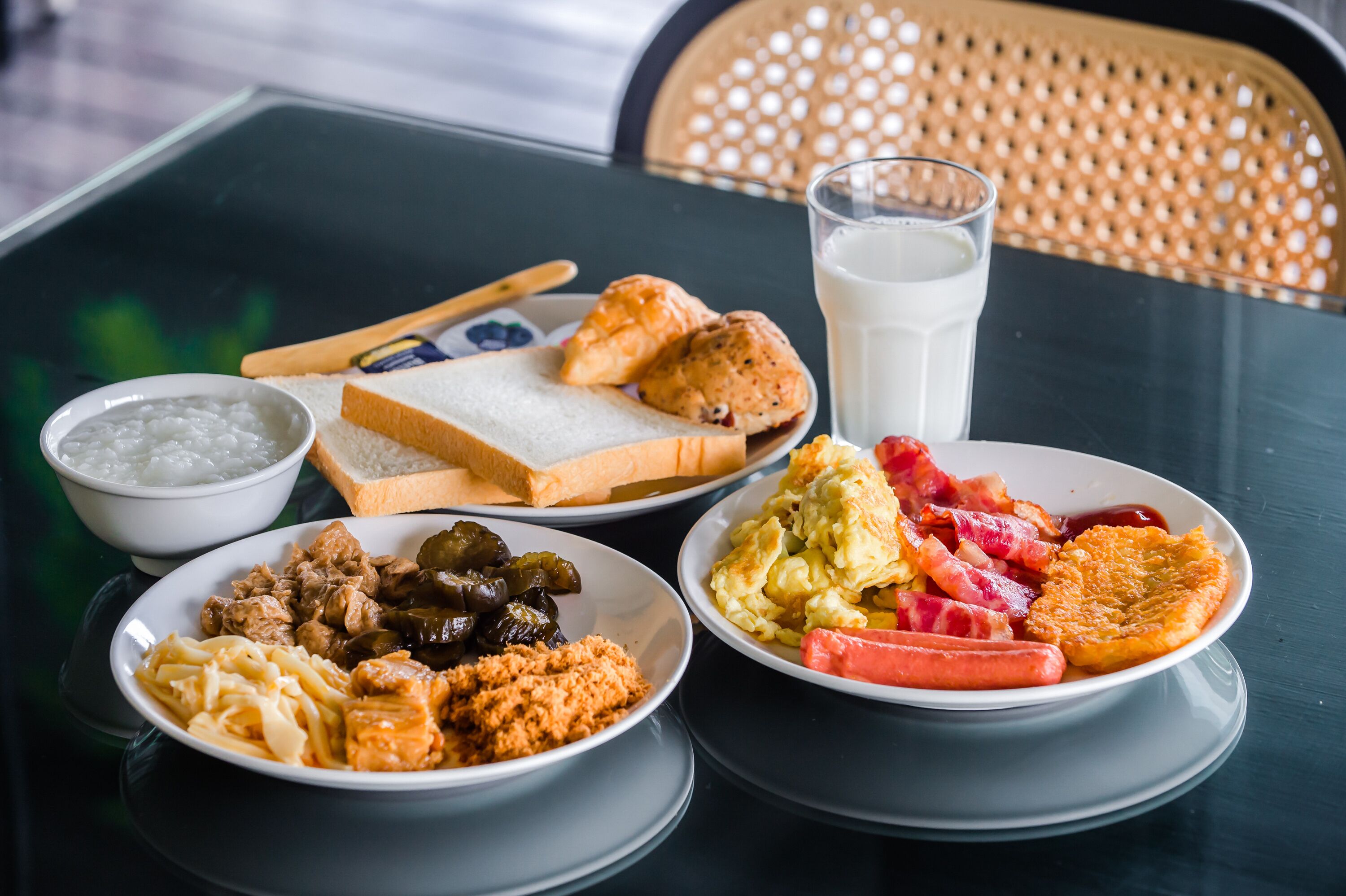 A table with various breakfast items including bread, eggs, sausages, and a glass of milk.