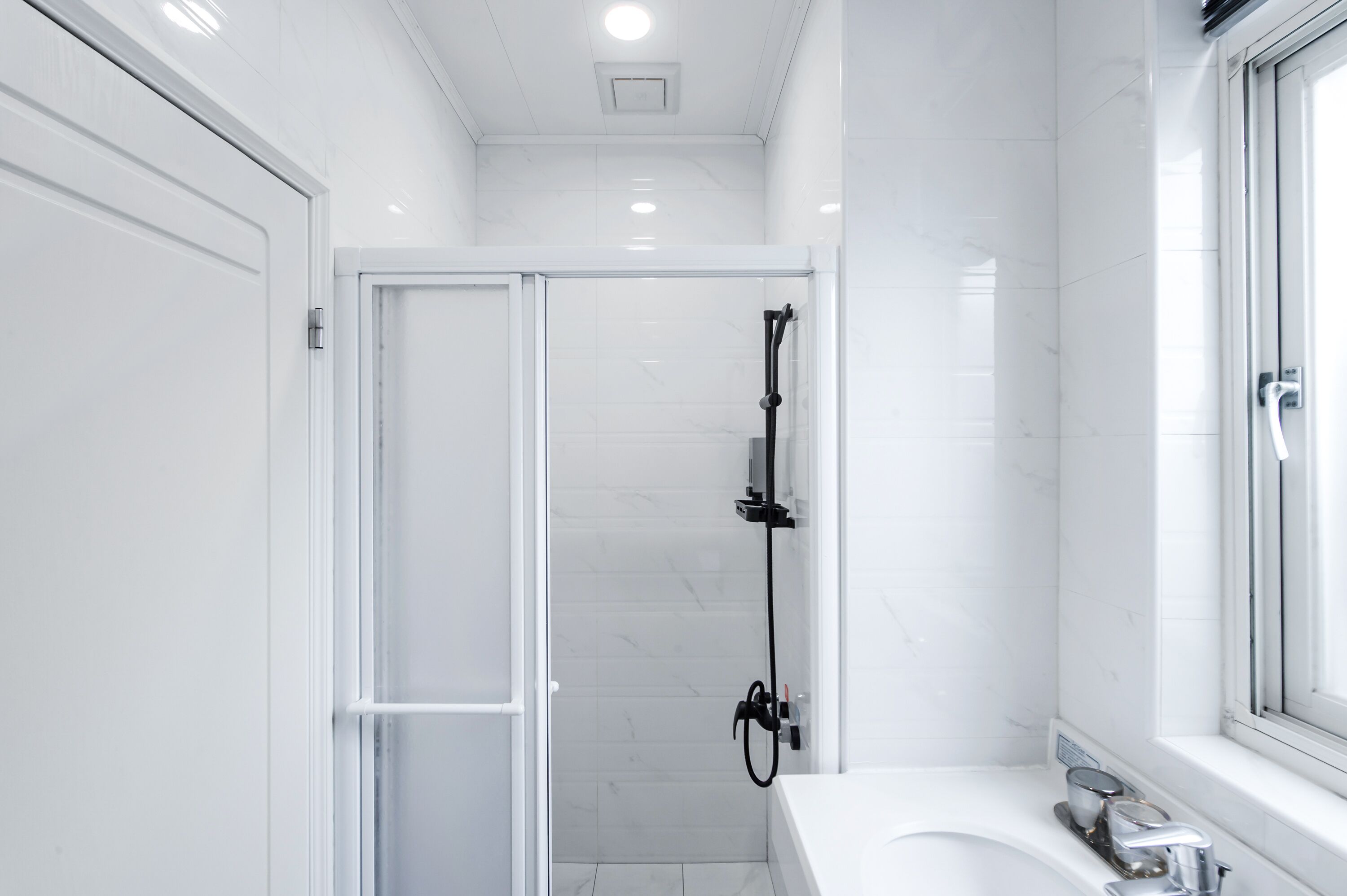 Une salle de bain moderne avec une douche à l’italienne en verre, un lavabo blanc et une fenêtre.