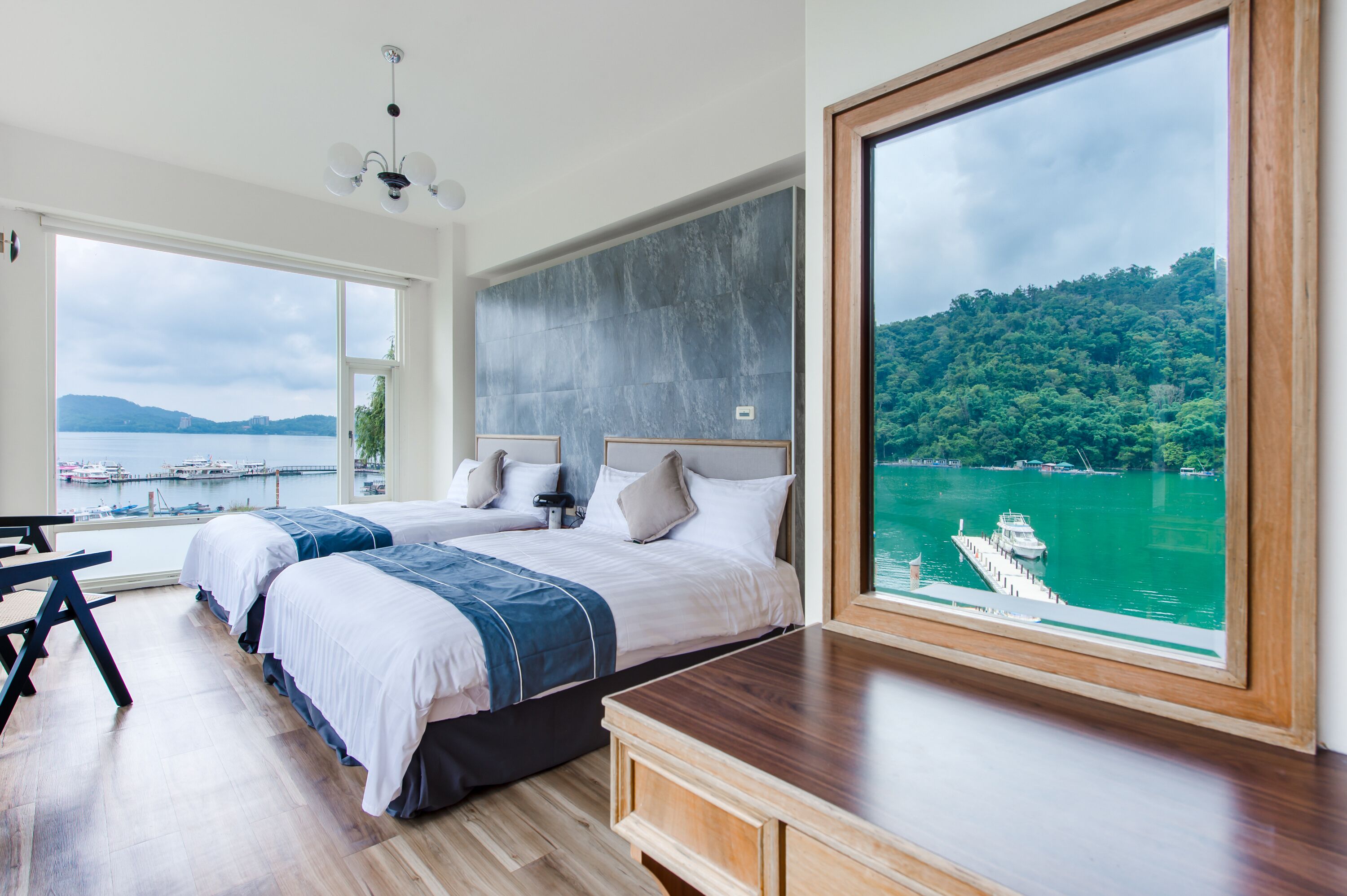 A modern hotel room with a large bed, a desk, and a view of a lake and boats.