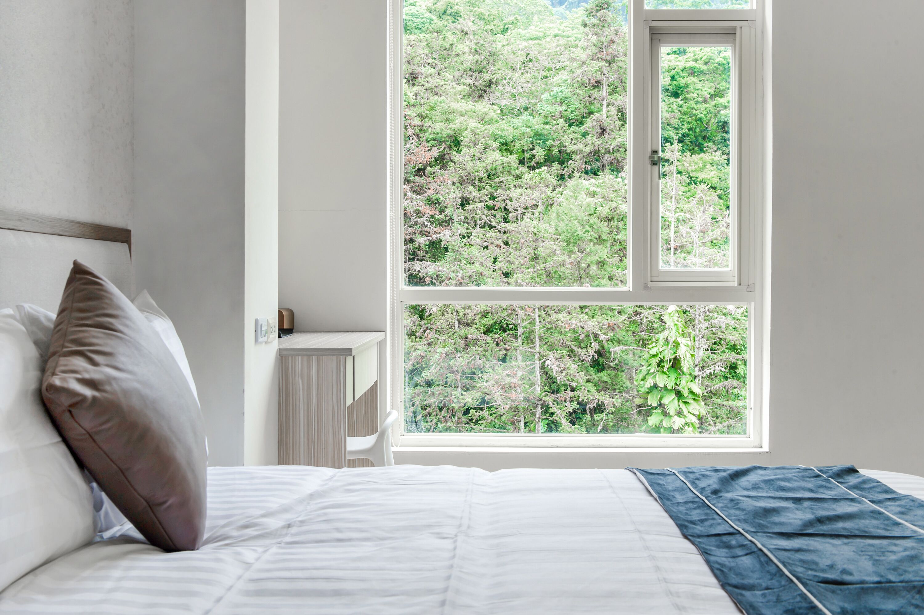 Un dormitorio con un ventanal grande, una cama y una mesita de noche.
