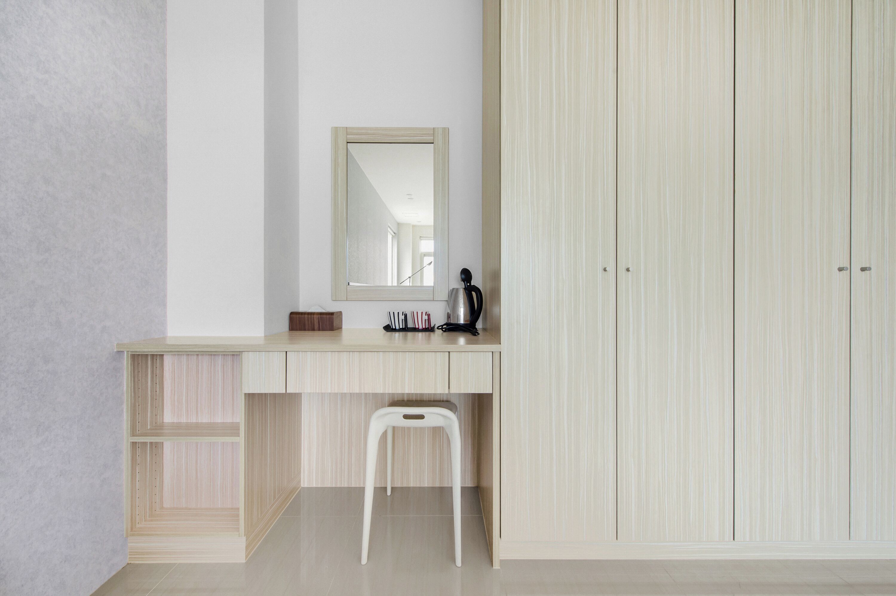 A minimalist room with a wooden desk, a white chair, a mirror, and a wardrobe.