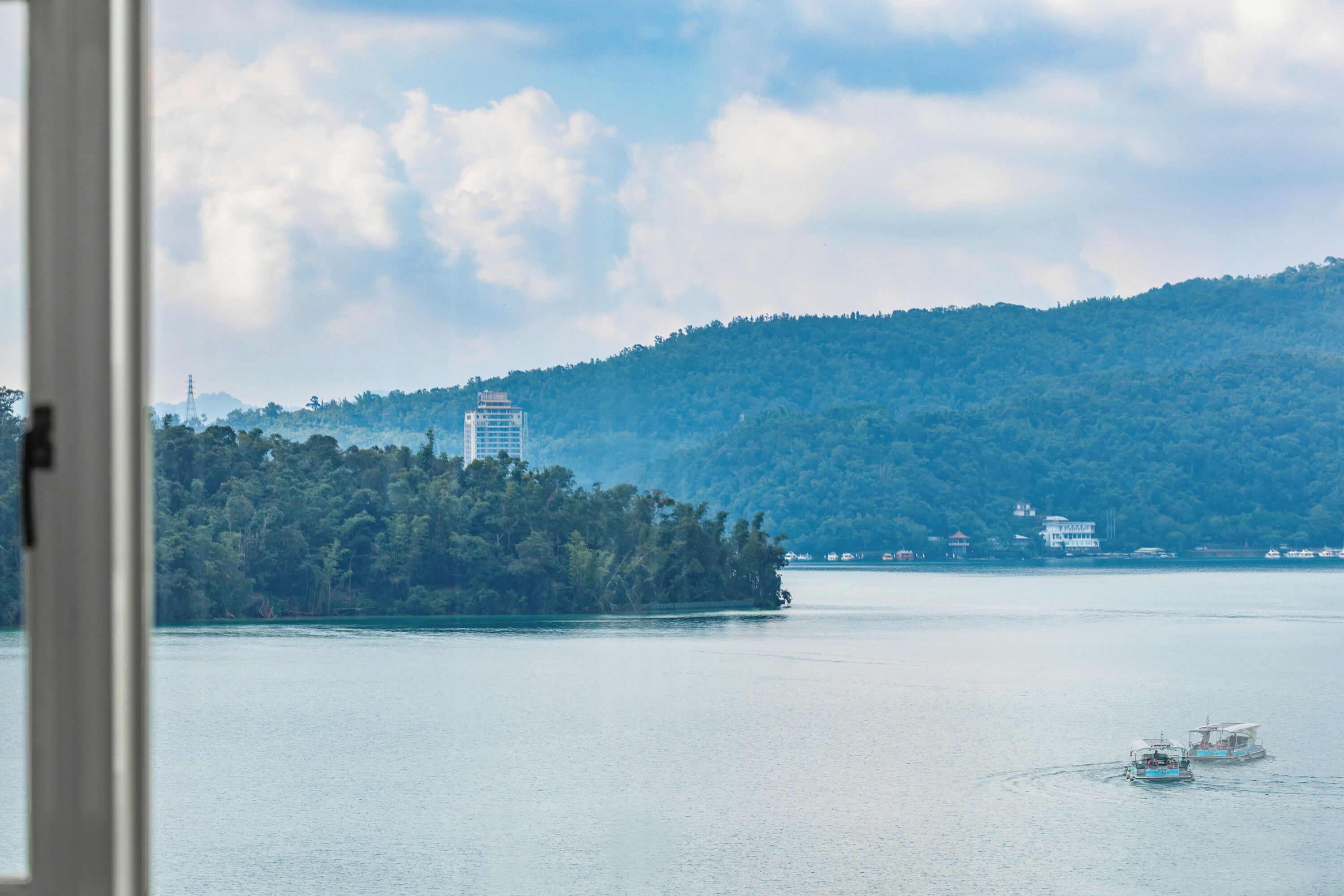 A view of a lake with a boat, a forested island, and a distant building.