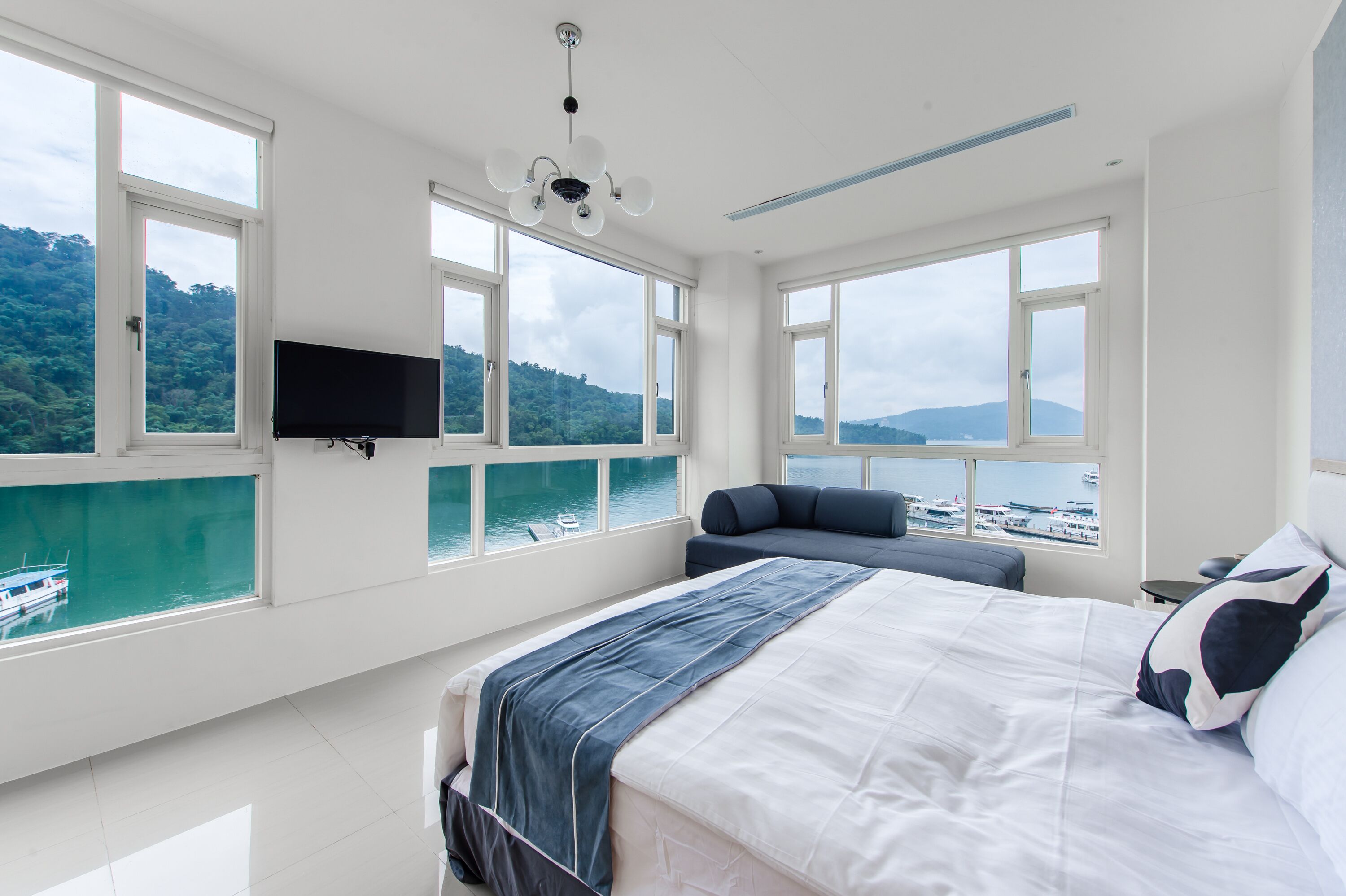 Une chambre moderne avec un grand lit, un téléviseur fixé au mur et une vue sur la mer grâce à de grandes fenêtres.