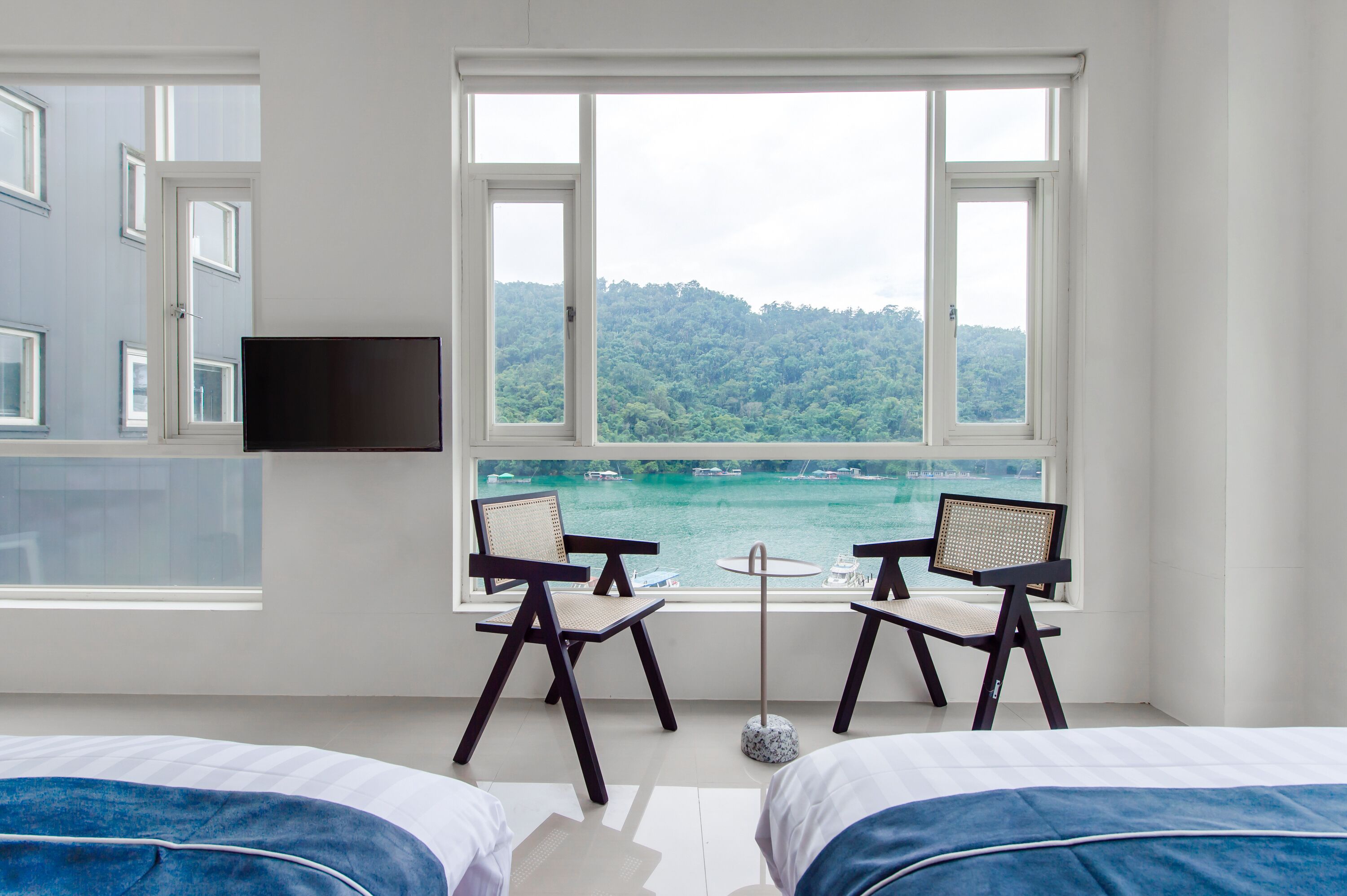 Habitación de hotel con dos camas, televisión y vistas a un lago y bosque.