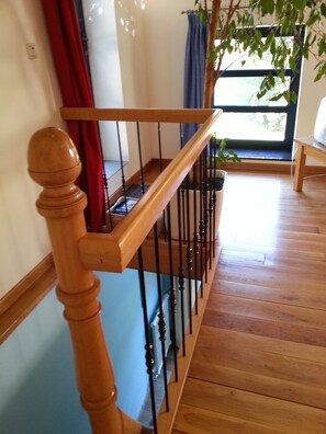 Un escalier en bois avec une rampe noire et un pot de fleurs placé sur le palier.