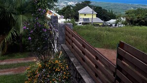 A scenic view from a balcony overlooking a coastal landscape, featuring a stone wall, wooden railing, and a variety of colorful flowers.