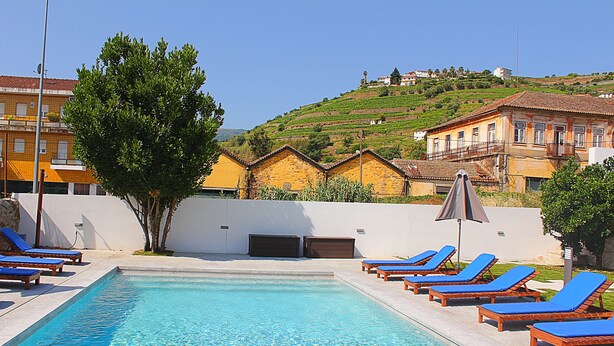 A swimming pool with blue lounge chairs and a tree in the foreground. - Casa do Salgueiral Douro (Peso da Régua)