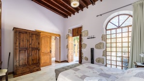 Une chambre avec un grand lit, une armoire en bois, un mur en pierre et une fenêtre donnant sur un beau paysage.