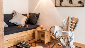 A cozy room with a wooden ceiling, a bed with pillows, a small table with a candle, a chair, and a rug on the floor.