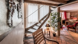A wooden staircase leading to a second floor, a dining area with a red curtain, and a potted plant.