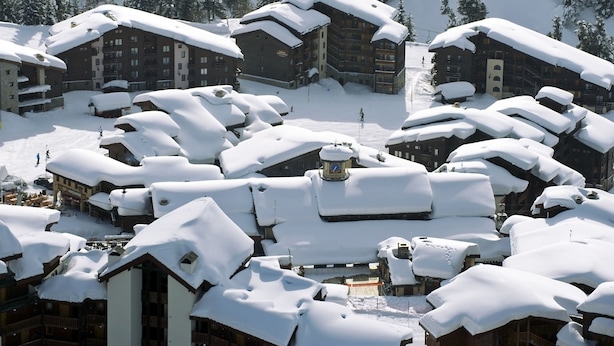A snow-covered resort with multiple chalet-style buildings, ski lifts, and a ski slope.