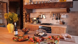 Een keuken met houten kastjes, een gasfornuis, hangende keukengerei en diverse etenswaren op het aanrecht.