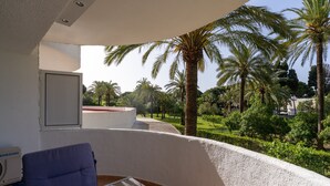 A room with a curved white wall, a blue chair, a Samsung air conditioner, and a view of palm trees and a garden. - Beachside studio Coronado (Marbella)