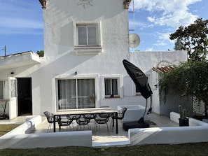 A white building with a patio area featuring a table and chairs, a satellite dish, and a potted plant.