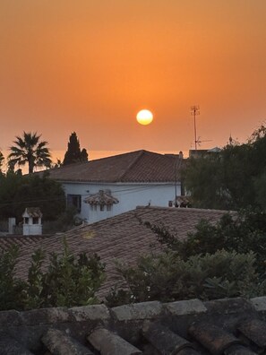 A sunset over a residential area with terracotta roofs and a white building with a traditional roof.