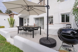 An outdoor patio with a table and chairs, a barbecue grill, and a large umbrella.