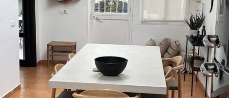Un comedor con una mesa blanca, sillas de madera, un tazón negro y una alfombra estampada.