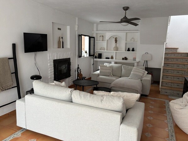 Una sala de estar con chimenea, sofás, televisor y ventilador de techo.