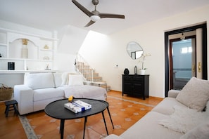 A living room with a sofa, a coffee table, a ceiling fan, a staircase, and a door leading to another room.