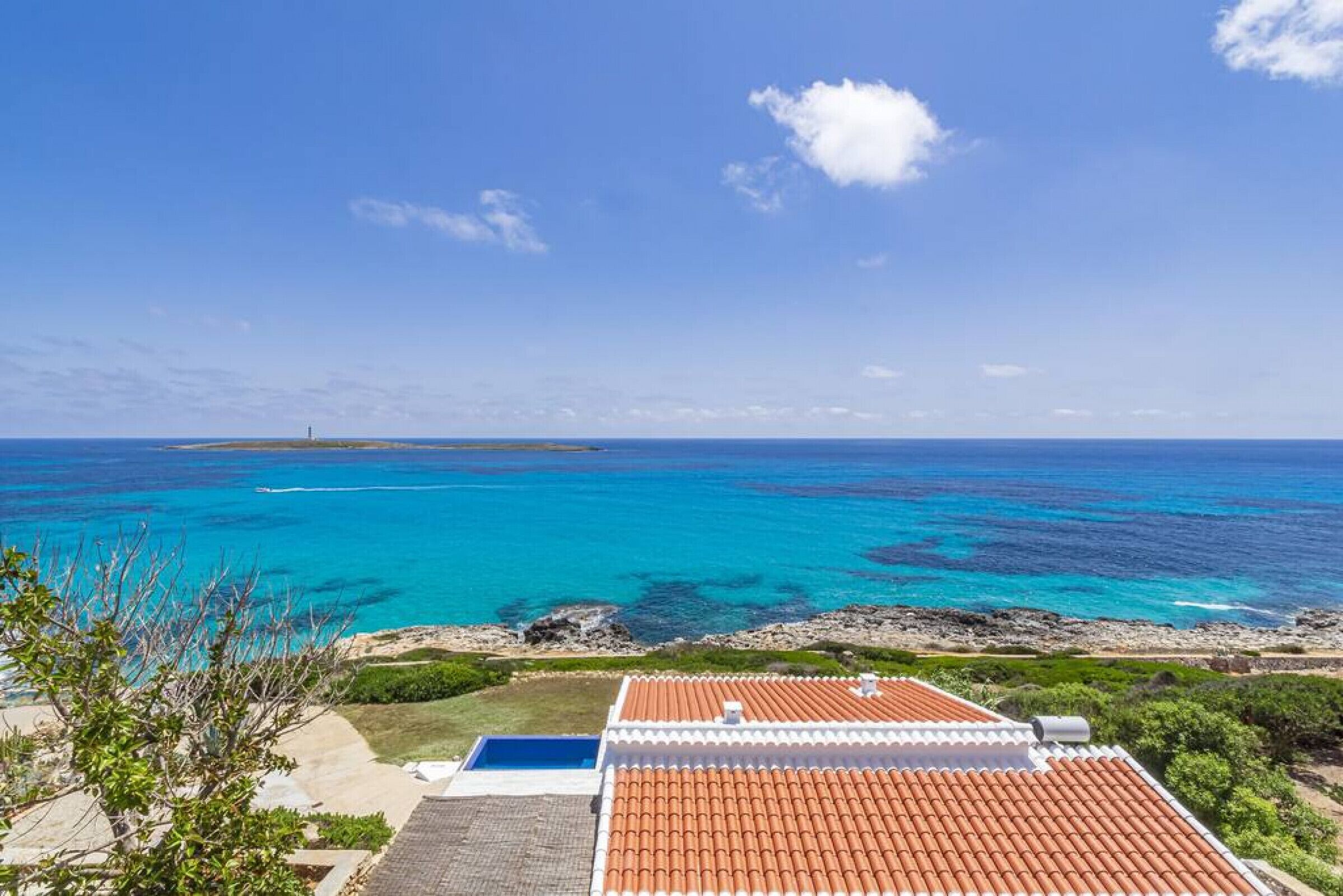 A coastal property with a red-tiled roof, a swimming pool, and a view of the ocean.