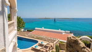 Vista a la piscina con un mar azul cristalino, un faro a lo lejos y un edificio con tejado de azulejos.