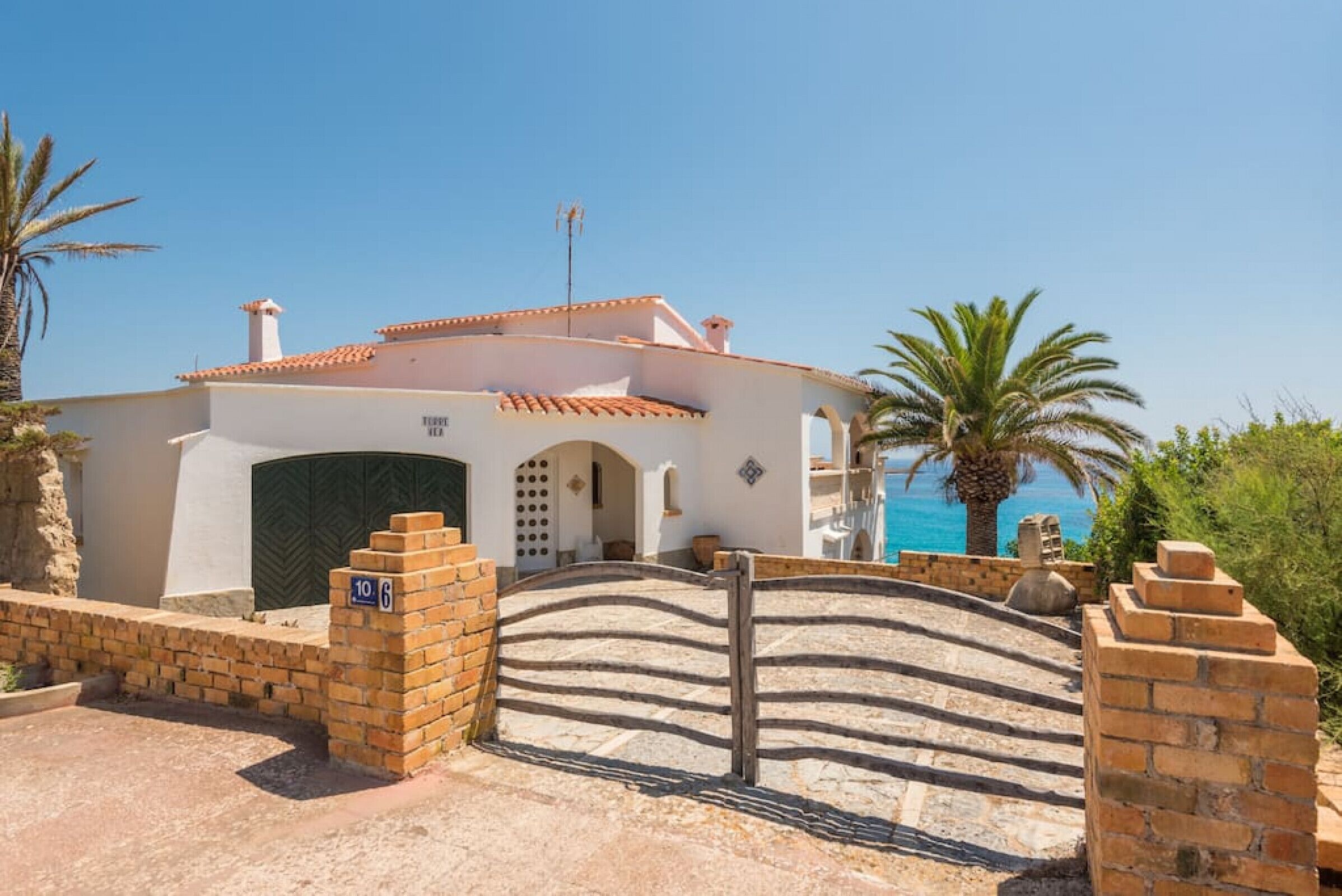 A coastal villa with a tiled roof, a gated entrance, and a view of the sea.