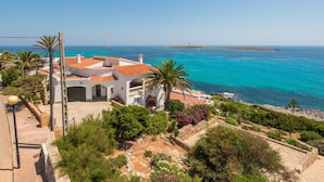 Una propiedad costera con un edificio blanco, techo de tejas rojas y vistas al mar.