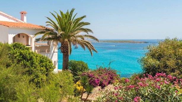 Vista costera con un edificio blanco, una palmera y mar azul cristalino.