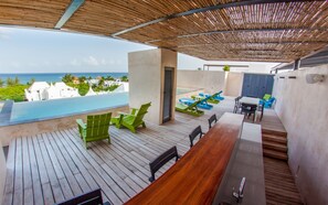 A wooden deck with a pool, outdoor seating, and a view of the ocean. - Stunning Design 2BR Condo in exclusive location by Happy Address (Playa del Carmen)