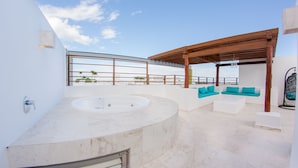 Een moderne buitenbadkamer met een jacuzzi, witte marmeren vloer en een houten pergola.