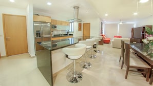 Een moderne keuken met een centraal eiland, roestvrijstalen apparatuur en een eethoek met barkrukken en een houten tafel.