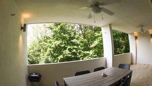 A covered patio with a table and chairs, a ceiling fan, and a view of lush greenery. - Luxurious 2BR Condo surrounded by nature by Happy Address (Playa del Carmen)