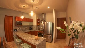 A modern kitchen with granite countertops, stainless steel appliances, and wooden bar stools. - Fabulous 3BR Condo steps away from 5th Avenue and beach by Happy Adddress (Playa del Carmen)