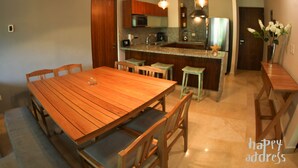 A modern kitchen with a wooden dining table, bar stools, and a built-in island. - Fabulous 3BR Condo steps away from 5th Avenue and beach by Happy Adddress (Playa del Carmen)