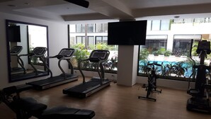 A gym with treadmills, a bench, and a rowing machine, with a large window overlooking a swimming pool. - Deluxe Studio in the best area of Playa Del Carmen by Happy Address (Playa del Carmen)